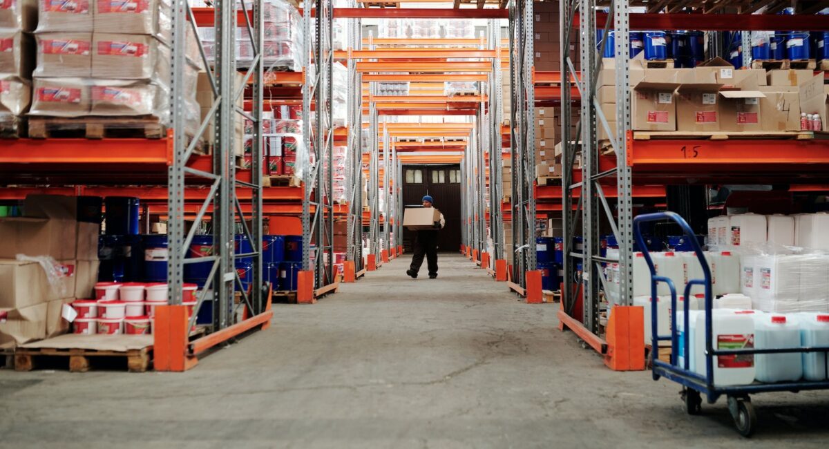 Man Standing in an Aisle of a Warehouse Carrying a Box