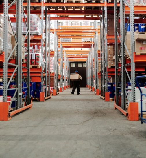 Man Standing in an Aisle of a Warehouse Carrying a Box