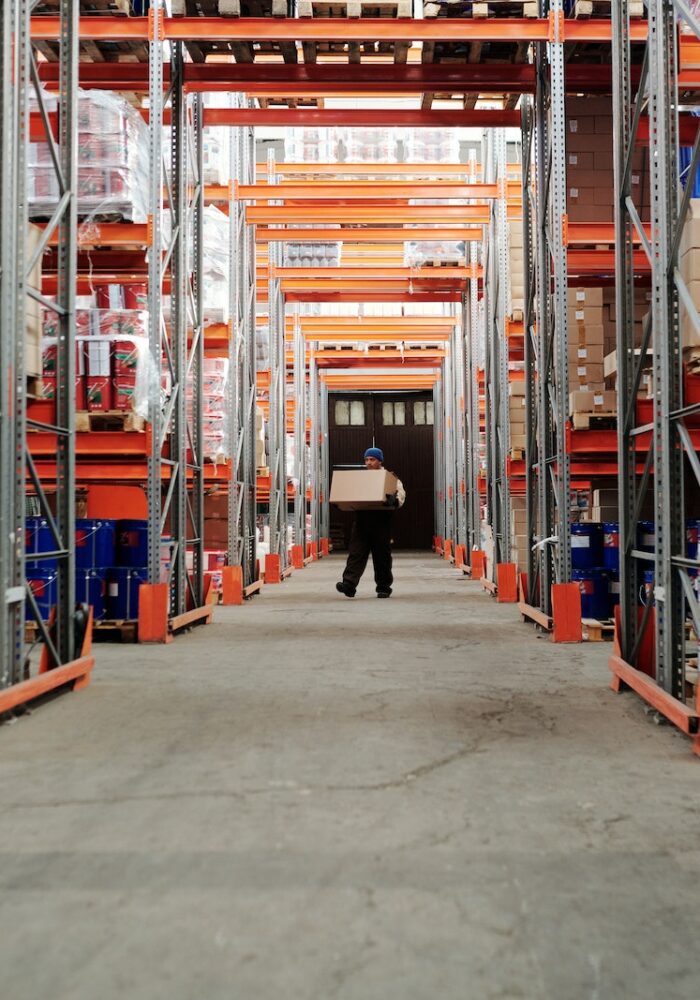 Man Standing in an Aisle of a Warehouse Carrying a Box